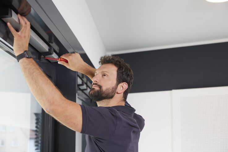 A service employee works on an automatic door using a screwdriver.