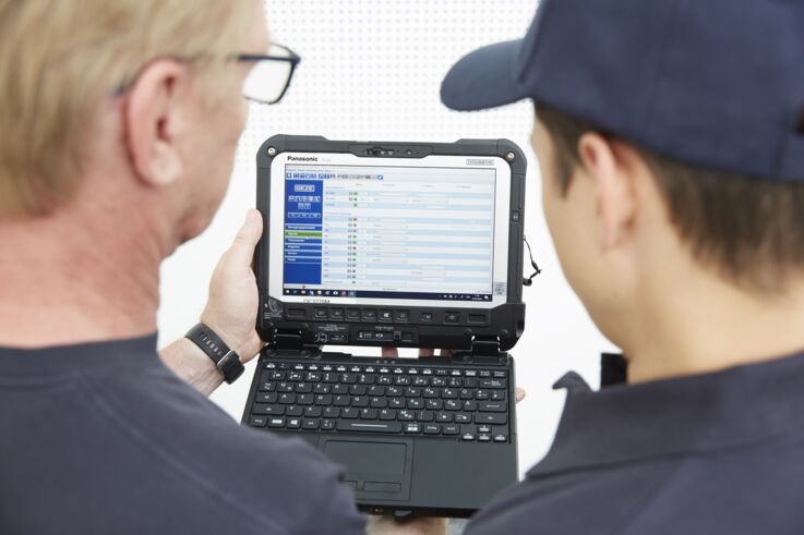 Ein Servicemitarbeiter und ein Kunde betrachten gemeinsam technische Daten auf einem robusten Laptop.