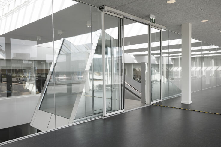 Ansicht eines Raumes mit geraden und schrägen Glasfronten und einer großen Glastüre