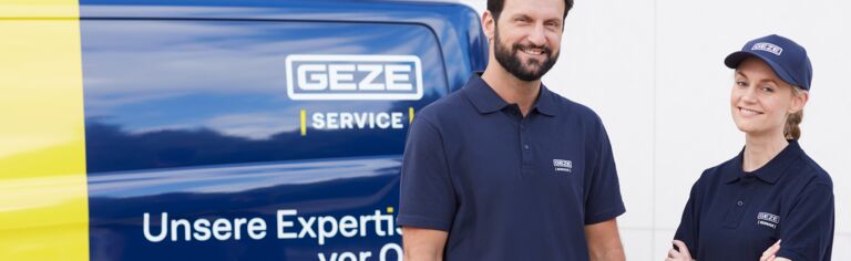 Zwei GEZE-Servicemitarbeiter in Firmenkleidung lächeln vor einem Servicefahrzeug.