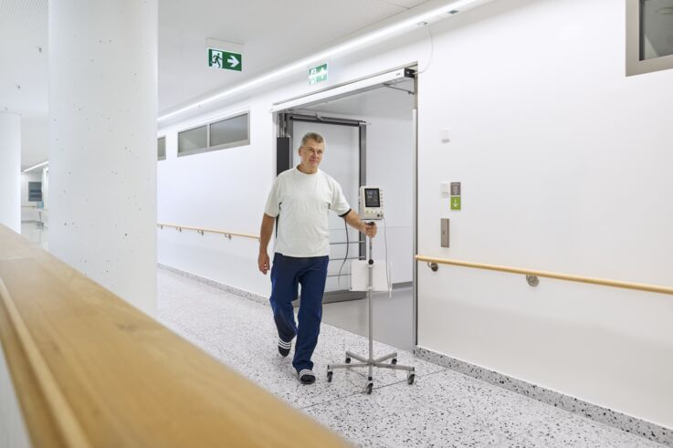 En pasient med en infusjon går gjennom en sykehuskorridor.