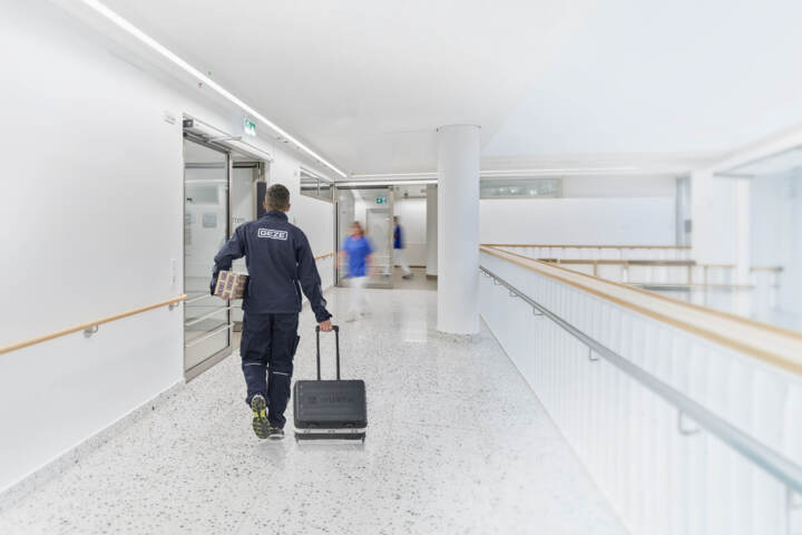Ein GEZE-Servicetechniker läuft mit Werkzeugkoffer und Türschließer durch einen hellen Krankenhausflur