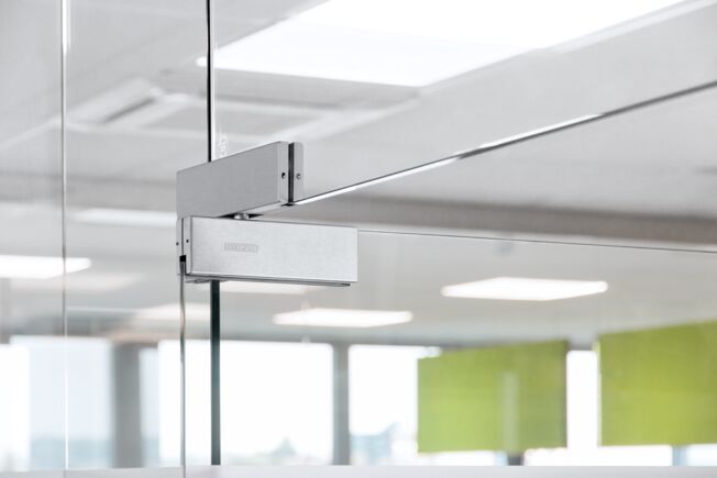 GEZE Patch Fittings Detailed view of the top floor-mounted pivot bearing with screw-out pivot bearing bolt on one all-glass door.