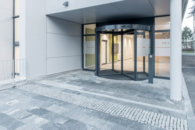 GEZE TSA 325 NT teliüveg forgójató, a Leonbergi Fejlesztési Központban beépítve A három- vagy négyszárnyú ajtókhoz alkalmazható, automatikus forgóajtó rendszer nem csak optimális átjárási kényelmet, hanem modern dizájnt is biztosít.