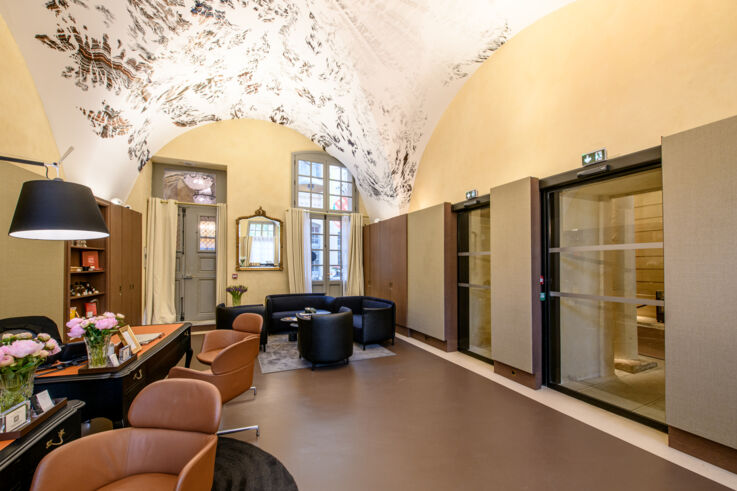 Hotellobby mit braunen und schwarzen Sesseln und Tischen und Glastüren rechts