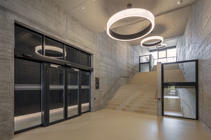 A large, modern entrance area with high concrete walls, automatic glass doors and a wide stairway. 