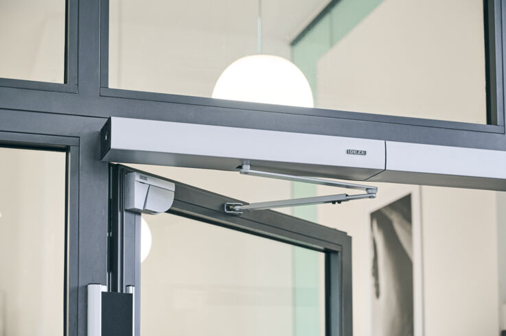 Automatic door closer on a glass door with black metal frame.