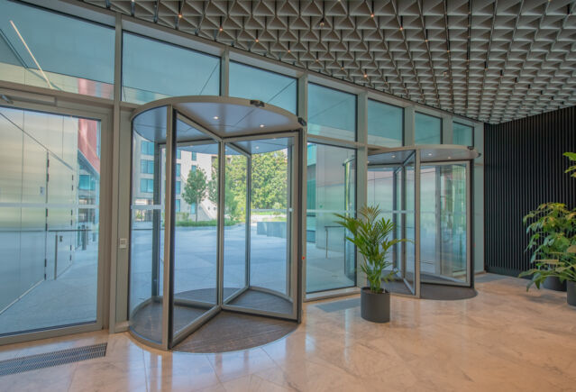 Deloitte Headquarter   Fokus auf den Lobbyeingang Innenansicht des Haupteingangs der Lobby mit zentraler Bepflanzung, die Offenheit, Ausgewogenheit und eine einladende Eleganz unterstreicht.