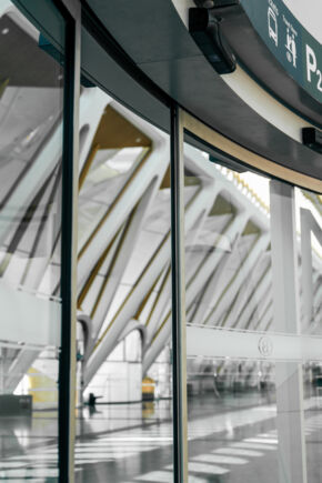Nærbilde av en buet skyvedør med innglassing, der hallen speiler seg