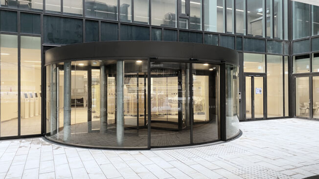 Rigshospitalet Dänemark Eine gewölbte Schiebetür aus Glas mit Slimdrive SC-Antrieb ist in die intelligente Glasfassade vor der Karusselltür des Patienteneingangs integriert.